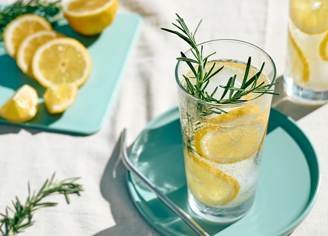 Ein Glas Zitonensirup mit Zitronenscheiben und Rosmarinzweigen.