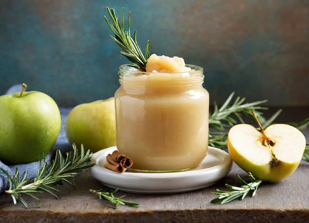 Apfelkompott im Glas mit Äpfeln und Rosmarinzweigen drumherum.